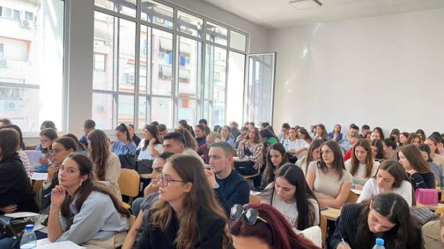 Rows of young people seated at desks in a lecture hall, taking notes