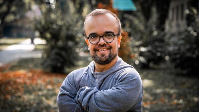 Portrait of a smiling man with glasses and a beard, arms crossed, in a park