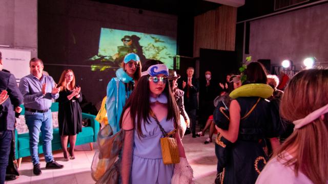 Models in outfits made from recycled textiles walk through an applauding audience at a fashion show