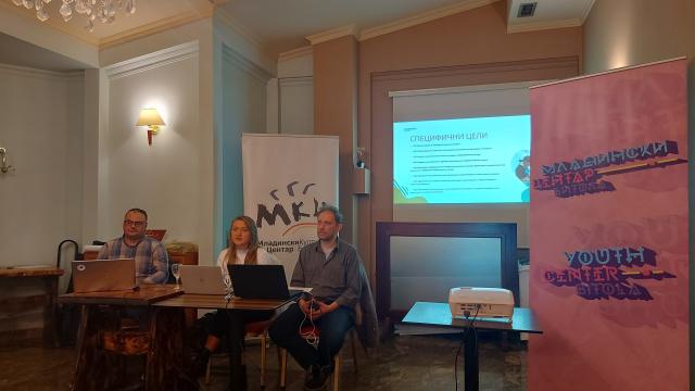 Three presenters at a table with laptops beside Youth Centre Bitola roll-up banners