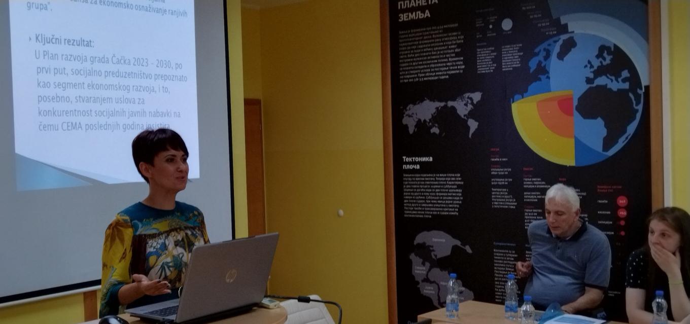 A woman presents from a laptop beside a projected slide while others listen