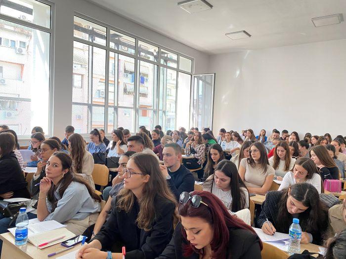 Rows of young people seated at desks in a lecture hall, taking notes