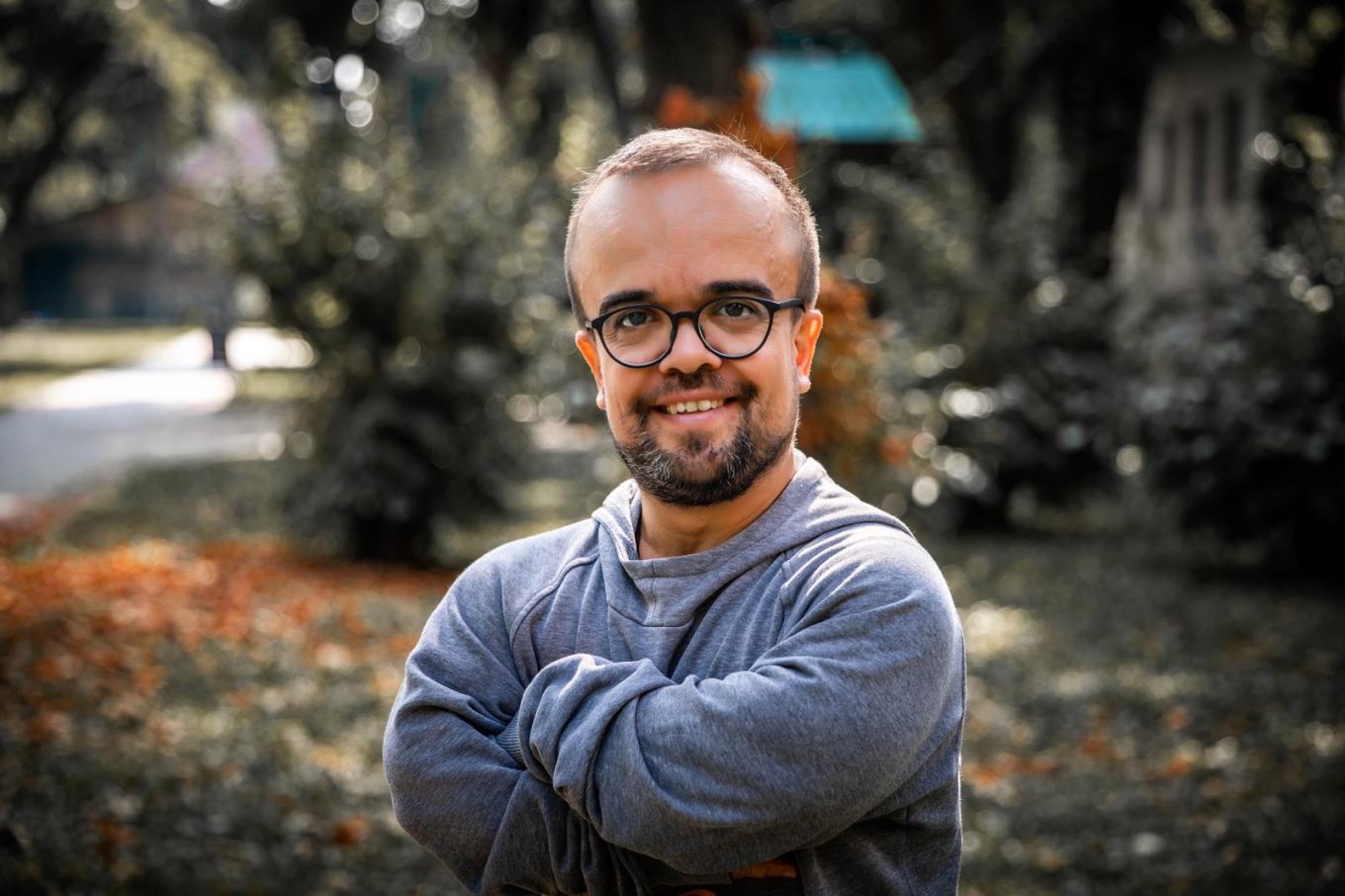 Portrait of a smiling man with glasses and a beard, arms crossed, in a park