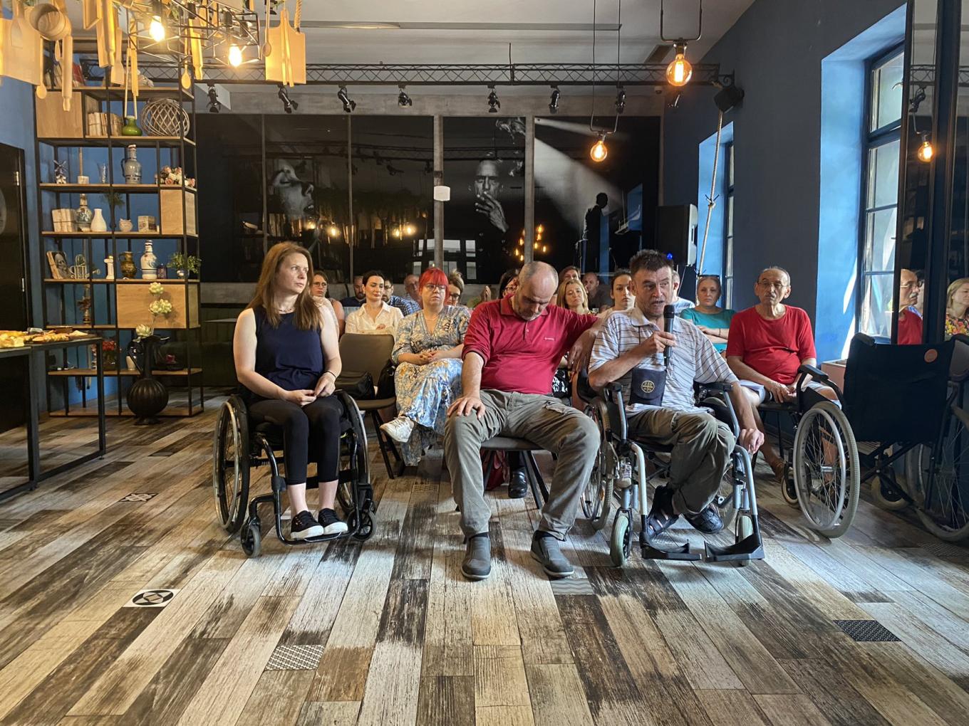 People, several in wheelchairs, seated in a café listening to a talk