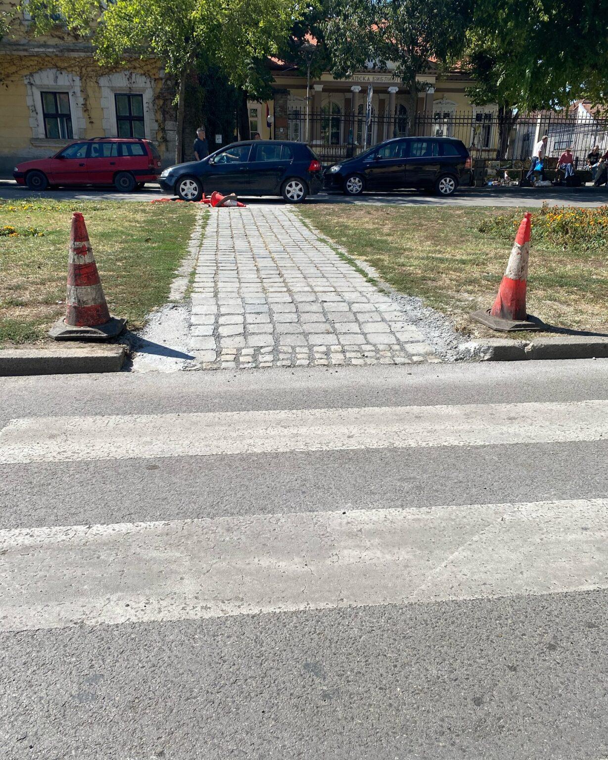 A pedestrian crossing leading to a paved path between traffic cones