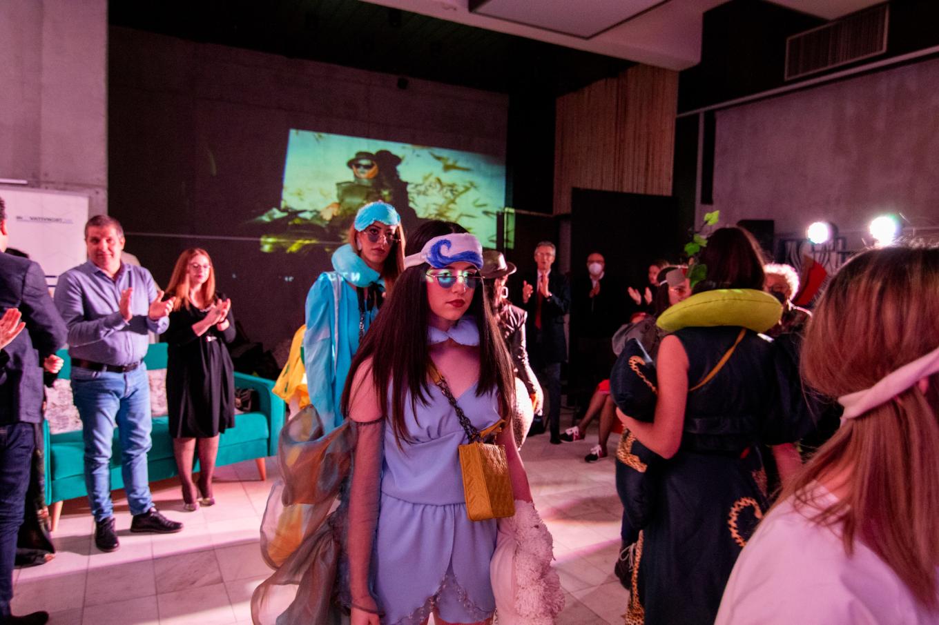 Models in outfits made from recycled textiles walk through an applauding audience at a fashion show