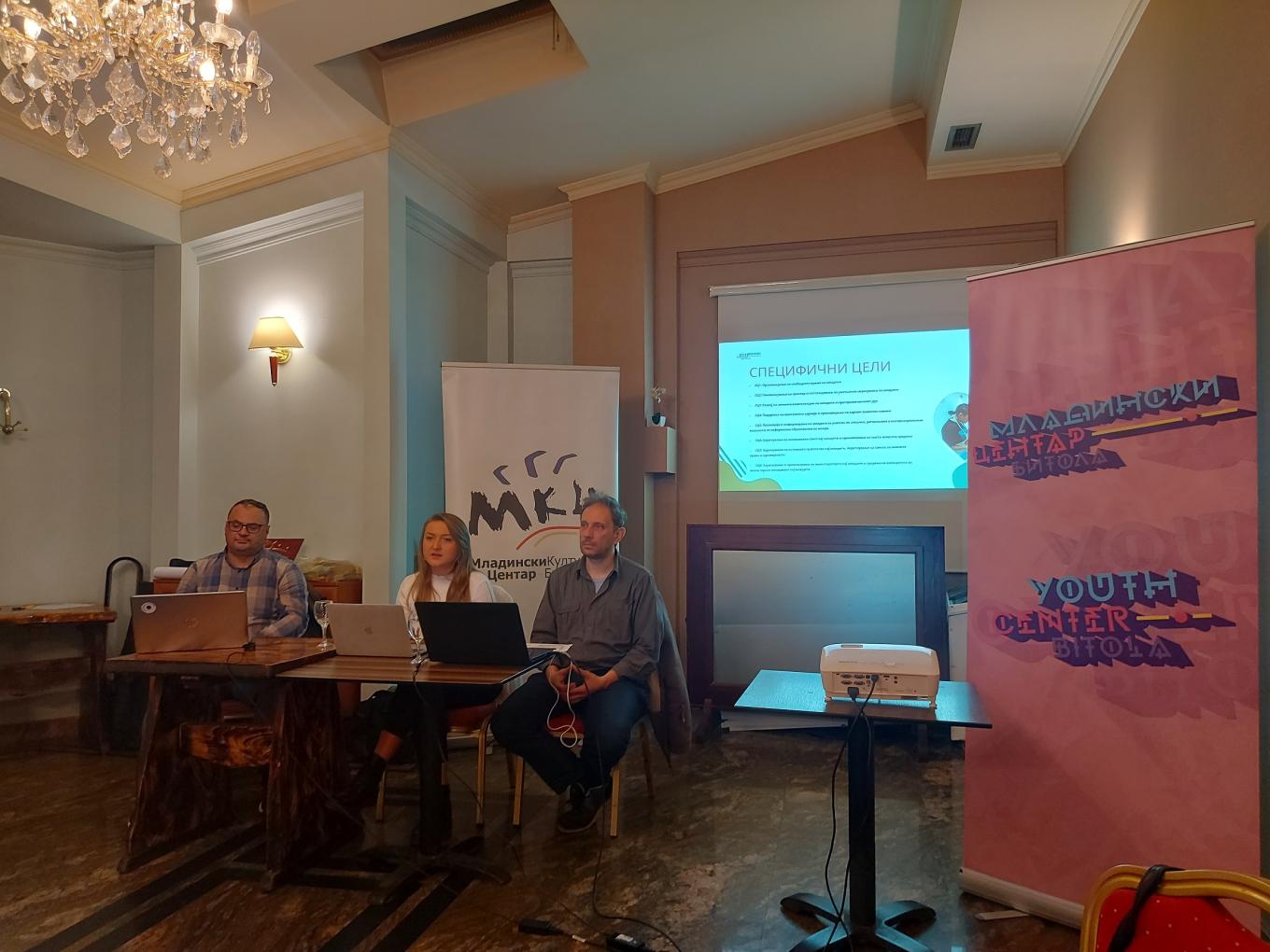 Three presenters at a table with laptops beside Youth Centre Bitola roll-up banners
