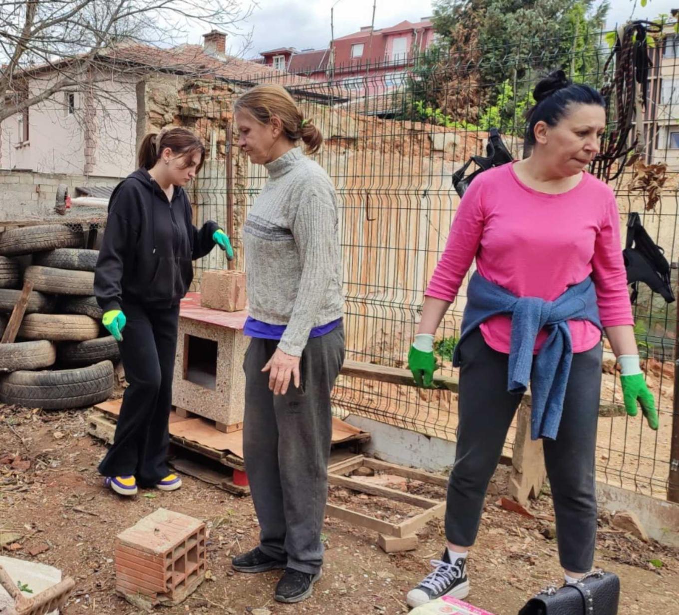 Three women in work gloves at an outdoor animal shelter